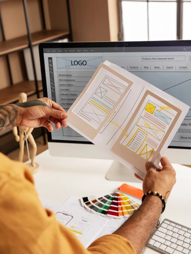 A web designer checking page layout and structure with his hand drawn layouts in a notebook.